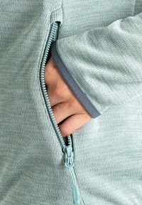 Hellgrüne, gepolsterte Jacke mit Reißverschluss aus strukturierter Stoff; verfügt über einen grauen Ärmelabschluss mit glattem Rand und eine Seitentasche. Der Reißverschluss ist aquafarben.