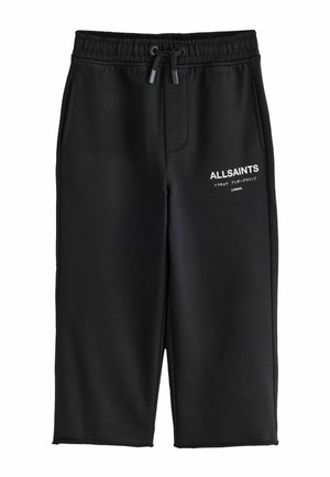 Blondes Kind trägt schwarzen AllSaints-Hoodie und passende Hose mit Logos, steht vor schlichtem grauem Hintergrund und schaut nach vorne.
