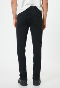 Jeans in denim nero con una vestibilità slim, caratterizzati da tasche posteriori standard e una texture liscia. La vita è semplice, senza chiusure visibili.