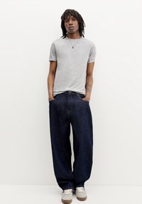 Un tricou gri cu mânecă scurtă, asortat cu blugi închiși la culoare, cu croială lejeră. Întregul outfit este completat cu adidași gri și accente hardware minime.
