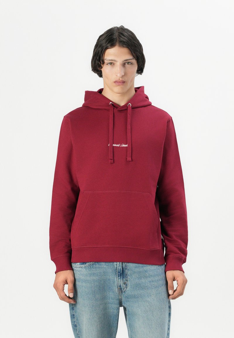Bordo spalvos megztinis-kapucha su priekiu kišeniu, raišteliu ant galvos ir balta logotipo detalė. Sukombinuotas su šviesiai mėlynomis džinsomis. Pagamintas iš medvilnės mišinio.