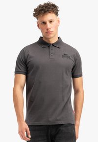 Šedé polo tričko vyrobené z bavlny, s límečkem, třemi knoflíky a krátkými rukávy. Na levé části hrudi se nachází černé logo.