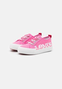 Baskets basses en toile rose avec des semelles en caoutchouc blanches, des lacets blancs et le logo "Levi's" en blanc sur le côté extérieur de chaque chaussure.