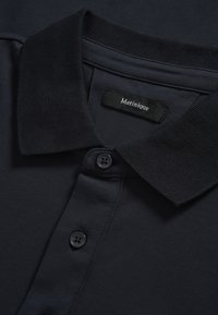 Polo azul marino con cuello acanalado, tapeta con dos botones y textura suave. Etiqueta de la marca "Matinique" visible en el interior.