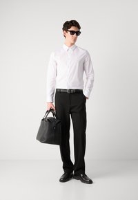 White button-up shirt, black trousers, black belt. Black textured bag with rolled top. Accessories include dark sunglasses and black shoes.