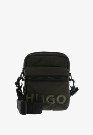 Bolso bandolera de nylon suave color verde oliva con cierre de cremallera, cuenta con un parche con el logo en la parte frontal y una correa ajustable con detalles metálicos.