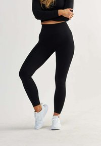 Leggings neri realizzati in materiale elasticizzato con vita alta. Abbinati a scarpe da ginnastica bianche, creano una silhouette elegante e aderente.