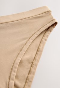 Primer plano de ropa interior de algodón beige con costuras visibles y cintura elástica sobre un fondo liso claro.