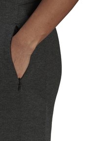 Dunkelgrauer Stoff mit weicher Textur, ausgestattet mit einer Seitentaschen mit Reißverschluss. Das Kleidungsstück schmiegt sich eng an den Körper und betont Form und Design.