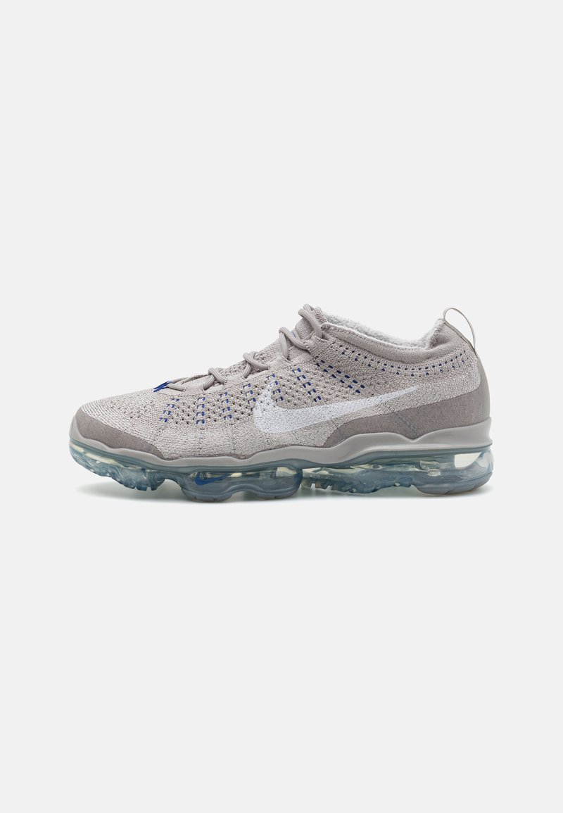 Light gray athletic shoes with a textured, knitted upper, blue accents, and a translucent air-cushioned sole. Nike Swoosh logo visible.