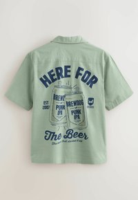 Vihreä lyhythihainen paita, jossa on sininen graafinen kuvasto olutkannuista ja tekstit: "TÄÄLLÄ OLUTTA VARTEN" ja "BREWDOG PUNK IPA."