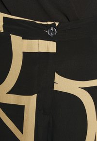 Czarna i beżowa tkanina w wzory o gładkiej teksturze, z zapięciem na guziki i abstrakcyjnymi elementami wzorniczymi.