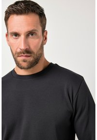 Czarna, długorękawowa koszulka typu crewneck wykonana z tkaniny bawełnianej, charakteryzująca się gładką teksturą i dopasowanym krojem. Brak widocznych wzorów czy elementów metalowych.
