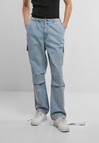 Světle modré denimové cargo kalhoty s uvolněným střihem, vybavené elastickým pasem, bočními kapsami a jemnými švy. Stylizované s bílými teniskami.