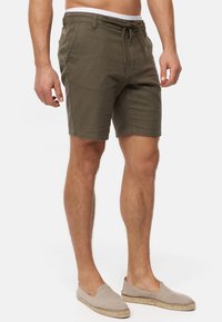 Shorts verts olive en tissu texturé, avec une taille élastique à cordon de serrage et des poches avant. Associés à des chaussures légères en toile beiges.