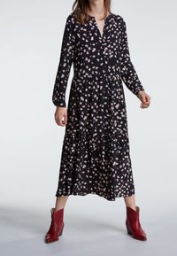 Czarna midi sukienka w kwiaty z długimi rękawami, dekoltem w kształcie litery V, marszczoną talią i warstwową spódnicą. Posiada różowe i białe wzory kwiatowe.