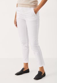 Baltas kokvilnas bikses ar slim fit, sānu kabatām un potīšu garumu. Pāris ar melniem slip-on apaviem. Gluda tekstūra un minimālisma dizains.