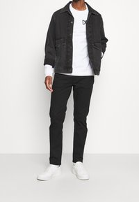 Svart denimjacka med krage, framfickor och knäppning över en vit sweatshirt. Svarta smalrandiga byxor och vita sneakers fulländar looken.