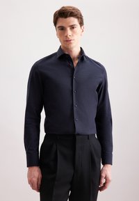 Granatowa, długosleeve koszula zapinana na guziki z ustrukturyzowanym kołnierzykiem, gładką fakturą i dopasowanymi ciemnymi guzikami; w połączeniu z dopasowanymi czarnymi spodniami.