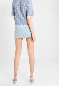 Light blue top with white floral embroidery and lace trim, paired with a ripped denim mini skirt. Stiletto heels complete the look.