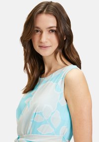 Ärmelloses Kleid aus hellblauem Stoff mit weißen Blättermustern. Glatte Textur mit enganliegendem Oberteil und ausgestelltem Rock.