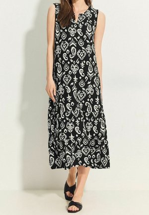 Czarna sukienka bez rękawów z białym wzorem paisley i diamentowym, o luźnym kroju sięgającym poniżej kolan. Płaskie czarne sandały.