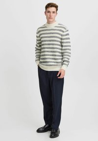 Pulover tricotat de culoare crem cu dungi bleumarin, având un guler și mânici cu model creponat. Asortat cu pantaloni largi bleumarin și pantofi negri.