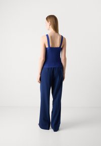 Top en tricot tissé bleu foncé à larges bretelles, corsage ajusté et dos ouvert ; associé à un pantalon long et ample bleu foncé.