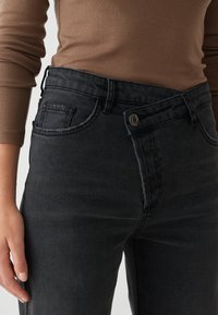 Donkerdenim jeans hebben een hoge taille, een design met vijf zakken en zilverkleurige elementen. De stof heeft een gladde textuur met een lichte vervaging.