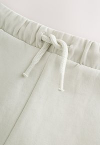Gros plan sur la taille d'un pantalon de survêtement beige clair avec une bande élastique et un cordon noué.