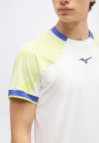 Κοντινό πλάνο ενός ατόμου που φοράει λευκό αθλητικό πουκάμισο με μανίκια με κίτρινες ρίγες και μπλε λεπτομέρειες γύρω από το γιακά και τις μανσέτες.