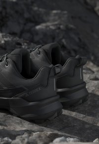 Paire de chaussures de trail Terrex noires reposant sur un terrain rocheux, montrant les vues arrière et latérales.