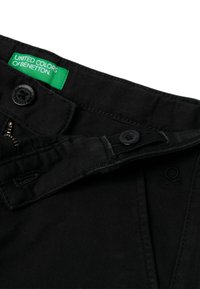 Černé džíny z denimu sZipem, dvěma knoflíky a zelenou nášivkou s nápisem "UNITED COLORS OF BENETTON." Jemně strukturovaná látka a vyšívané logo.