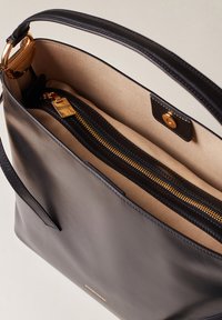 Schwarze Ledertasche mit goldfarbener Reißverschluss, beigem Innenfutter und Druckknopfverschluss. Verfügt über einen einzelnen Tragegurt und ein minimalistisches Design.