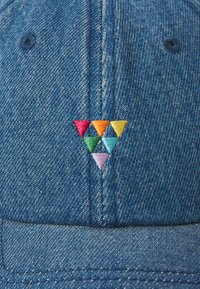 Denim sapka, amelyen elöl egy vörös, narancs, zöld, kék és lila színű háromszög alakú hímezett minta található, kontrasztos varratokkal.