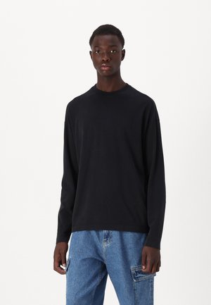 T-shirt nera a maniche lunghe in cotone morbido, con scollatura a girocollo e vestibilità comoda. Indossata con pantaloni cargo in denim blu.