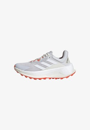 Zapatilla deportiva de color gris claro con parte superior de malla transpirable, diseño de tres rayas blancas y suela de goma naranja para tracción.