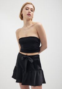 Haut noir sans bretelles avec une texture froncée associé à une jupe noire à volants avec un nœud noué à la taille, fabriquée en tissu lisse.