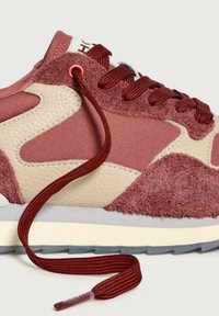 Närbild av en röd och beige sneaker med strukturerade mocka- och läderpaneler, med otasade röda skosnören som sträcker sig utåt.