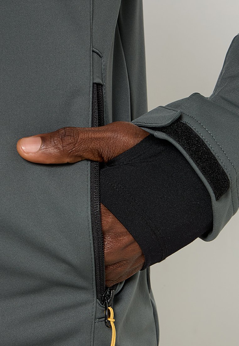 Veste gris foncé avec une poche zippée, dotée d'un poignet noir avec Velcro. Texture de tissu lisse avec des couleurs contrastées.