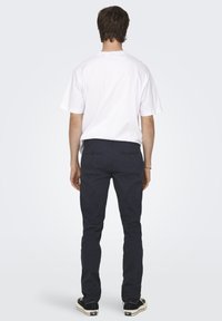 Camisa de algodón blanca, pantalones azul marino con bolsillos traseros, zapatillas negras. Diseño simple, corte relajado, sin patrones ni logotipos visibles.
