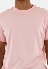 T-shirt in cotone rosa chiaro con maniche corte, scollatura a girocollo e piccolo logo bianco sul petto. Tessuto morbido e design aderente.