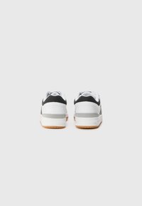 Hvide sneakers med sorte accenter, udstyret med en struktureret bagpanel, gummisål og polstret krave for komfort. Bageste udsigt vist.