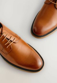 Chaussures en cuir marron avec une finition lisse, design à lacets, bout arrondi et semelle contrastante avec des détails de couture noire.