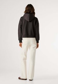 Felpa nera corta con cappuccio, abbinata a jeans bianchi a gamba larga. Presenta una vestibilità comoda e cuciture visibili sui pantaloni.