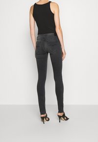 Top negro de tirantes combinado con jeans ajustados gris oscuro. Los jeans presentan un corte slim y bolsillos traseros con sutiles detalles de costura. Zapatos de tacón alto visibles.