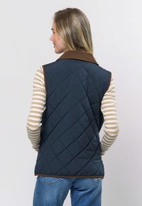 Marineblå quiltet vest med brun cordfløyelskjerne, lagd oppå en lys stripete langermet skjorte. Minimal metallbeslag og en avslappet passform.