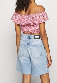 Rood en witte bloemen off-shoulder crop top met een gerimpelde halslijn, gedragen met lichtblauwe denim shorts met een rafelige zoom en achterzakken.