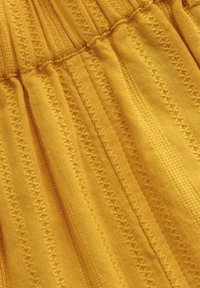 Tessuto a maglia giallo con righe verticali e motivi a diamante, caratterizzato da una consistenza morbida e dettagli arricciati in vita.