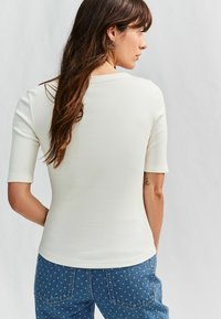 Vitt ribbat kortärmat plagg med rund halsringning, kombinerat med blå denimbyxor med vita prickar, som framhäver en figursydd silhuett.